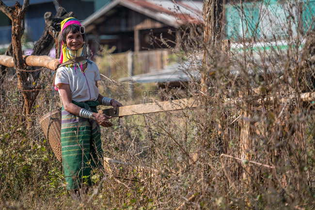 PADUANG PEOPLE, PAN PET VILLAGE, KAYAH STATE, MYANMAR - 28 January 2019: Portrait of local lady wearing brass coils placed around the neck, appearing to lengthen it, closing garden fence.