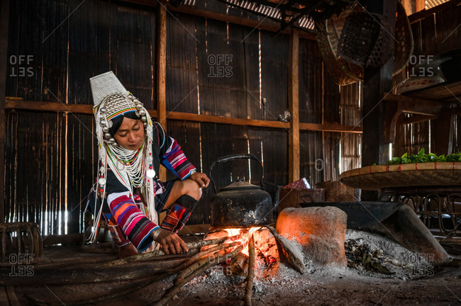 AKHA HILL TRIBE, HOKYIN VILLAGE, MYANMAR - 19 November 2019: Woman in traditional costume boils kettle to make tea on open wood fire.