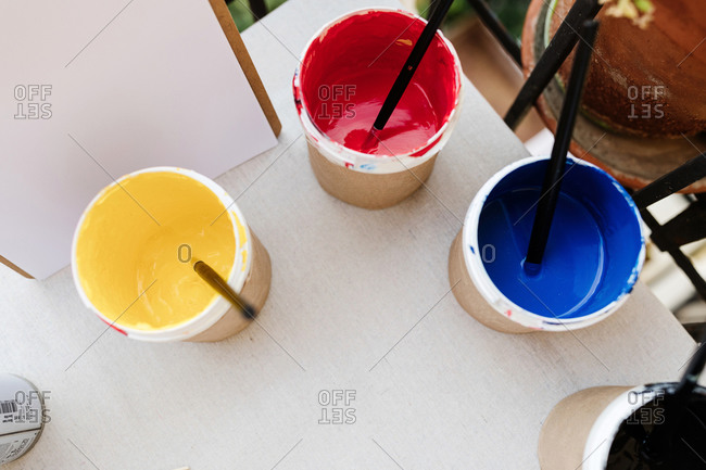 From above of set of paints of various colors and paintbrushes arranged on table in creative art studio