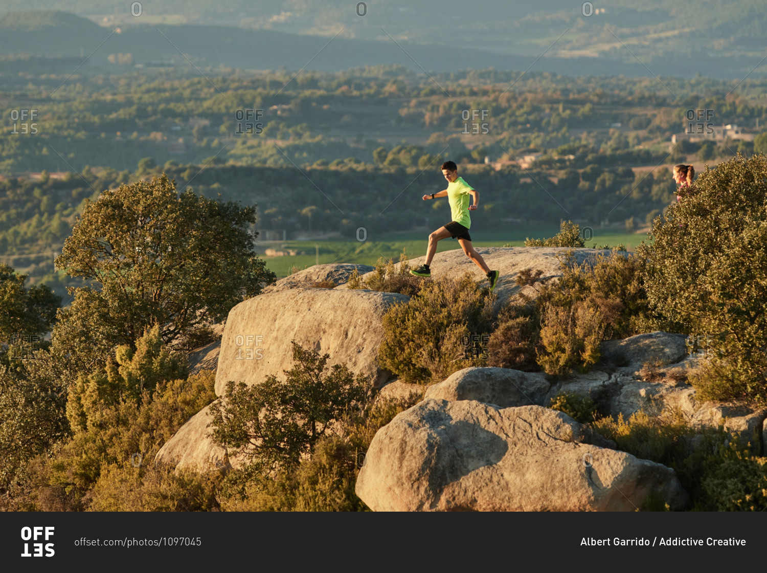 Side view of slim male runner jumping on rocks in mountains at sunset in evening during active training