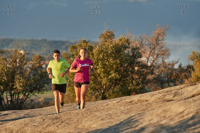 Sportsman and sportswoman running on slope in highland terrain during cardio training at sundown in summer