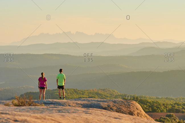 Remote view of sportsman and sportswoman standing on hill and having break during training in mountains at sunset