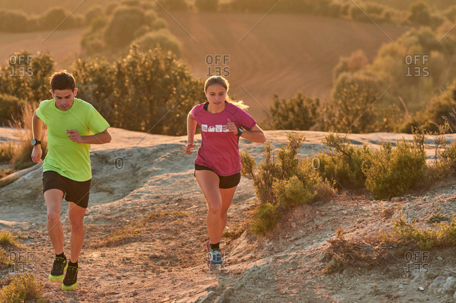 Sportsman and sportswoman running on slope in highland terrain during cardio training at sundown in summer