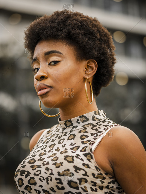 Low angle of confident stylish young African American female with curly hair dressed in jeans and crop top with animal print looking at camera while standing on urban street