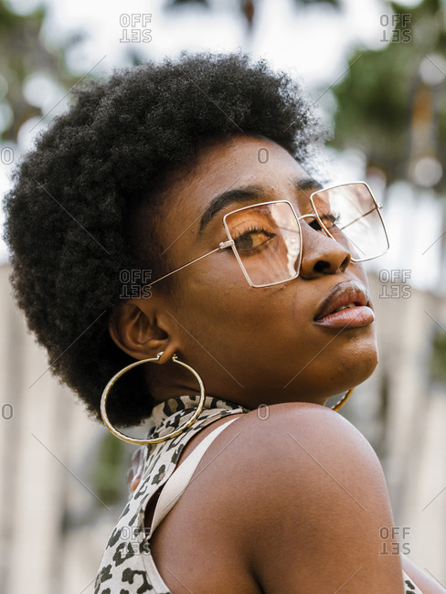 Confident stylish young African American female with curly hair dressed in jeans and crop top with animal print n casual outfit and trendy sunglasses looking at camera while standing on urban street