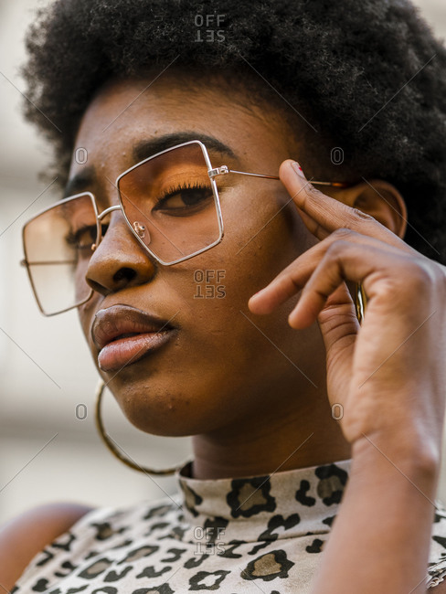Confident stylish young African American female with curly hair dressed in jeans and crop top with animal print n casual outfit and trendy sunglasses looking at camera while standing on urban street