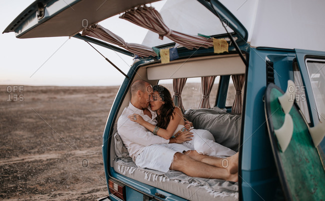 Gentle couple of travelers relaxing in van and tenderly hugging while enjoying vacation in savanna in summer