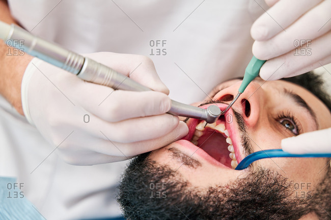 From above of unrecognizable dentist with explorer and dental mirror checking teeth of patient during appointment in modern clinic
