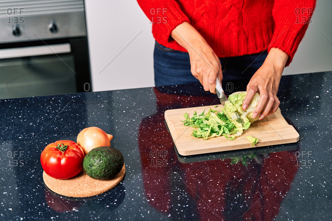 Crop faceless female cook cutting lettuce while preparing healthy vegetarian salad in kitchen