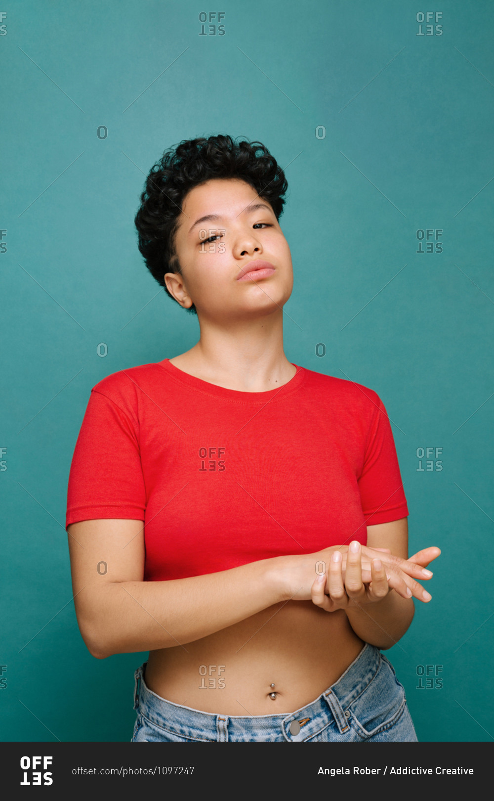 Young Latina woman holding her own hands with a red t-shirt, media shot, isolated vertical photo, tidewater green background