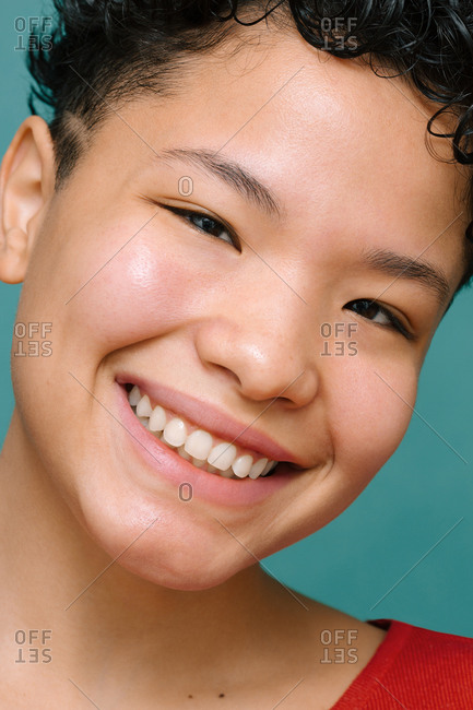 Portrait of young Latina woman with Asian eyes looking at the camera and smiling, close-up, isolated vertical photo, tidewater green background
