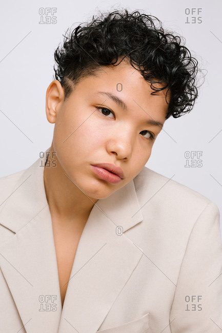 Young Latina woman with her head bowed, wearing a beige blazer. Isolated vertical photo, white background