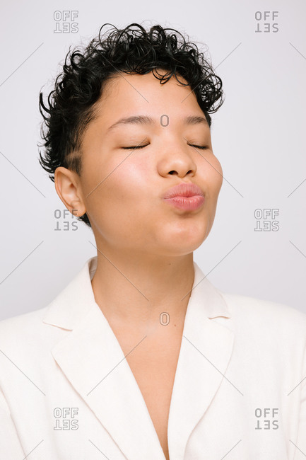 Young Latina woman making kissing gesture and closed eyes, isolated vertical photo, white background