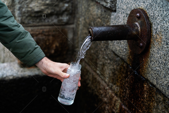 Side view of crop anonymous traveler filling bottle with potable spring water while hiking in Sierra de Madrid in Spain