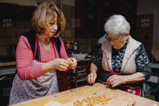 Busy senior women standing at table and preparing traditional domestic tortellini for dinner at home