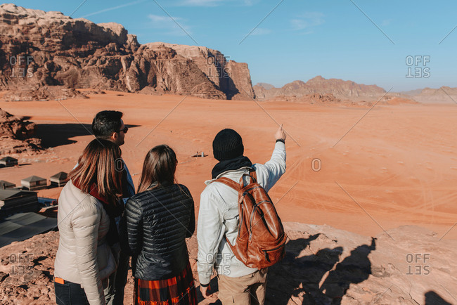 Back view of group of traveling friends standing in sandstone valley Wadi Rum and observing amazing landscape