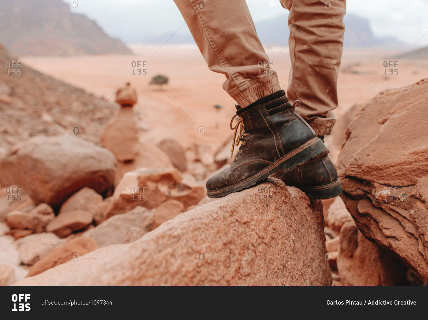 Legs of crop male tourist in hiking boots standing on rocks in Wadi Rum sandstone valley during holiday in Jordan