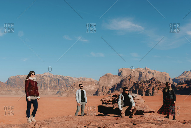 Company of tourists standing on rough rock in Wadi Rum sandstone valley and observing scenery on sunny day during vacation