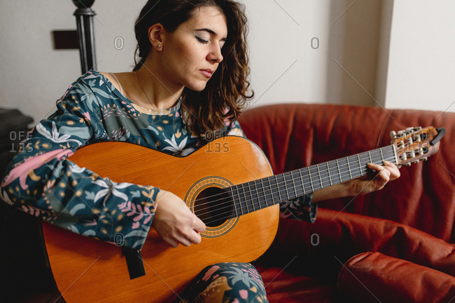 Close-up woman hands holding a guitar. Casual girl practicing and playing the instrument next to a fireplace. Cozy, hobby, domestic life, relax concept.