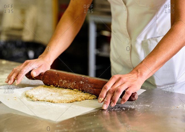 Crop unrecognizable pastry chef rolling short crust dough on baking paper while preparing cookies in kitchen