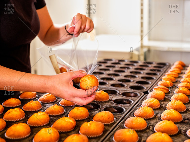 Crop anonymous baker packing freshly baked and cooled muffins into plastic bag while working in professional bakery