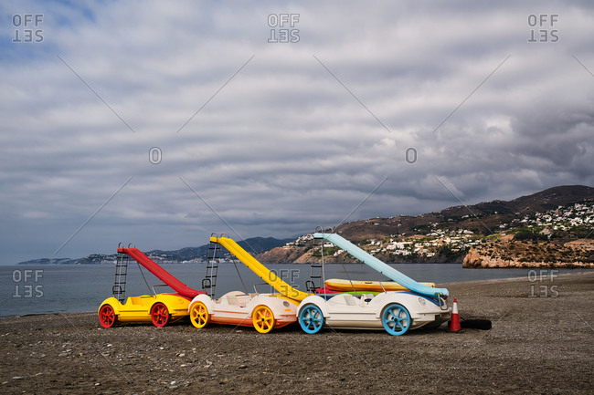 Collection of colorful pedal boats with slides placed on sandy beach on background of pink sunset over sea in Spain