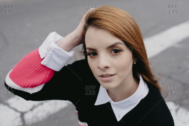 High angle of carefree female with red hair and in casual outfit standing in city street and looking at camera