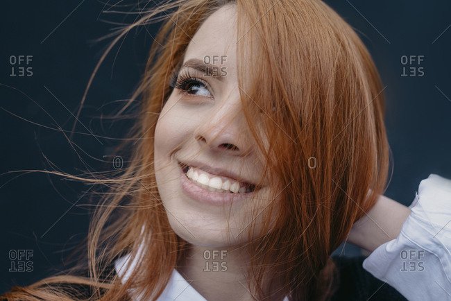 Young content redhead female with wind in hair standing in city and looking at camera
