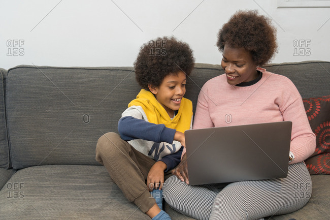 Content African American mother and son sitting on sofa with laptop and choosing movie for watching while spending time together at home