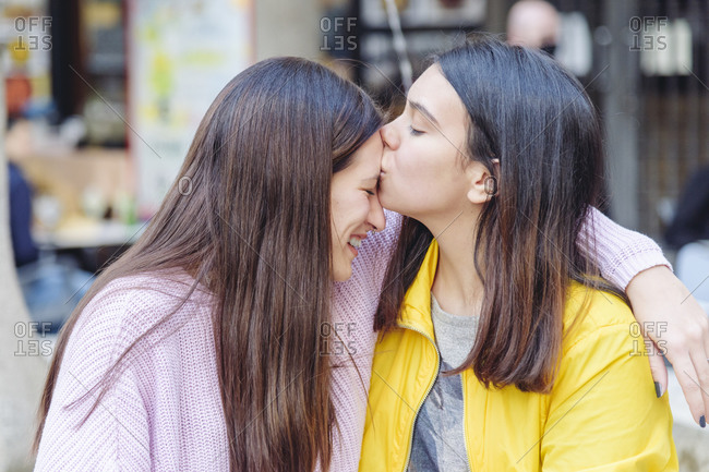 Side view of gentle lesbian woman kissing smiling girlfriend in forehead while cuddling in city and enjoying weekend