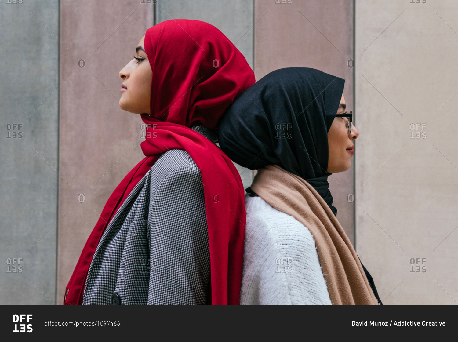Side view of Arab female friends in traditional hijab standing back to back on street and looking away
