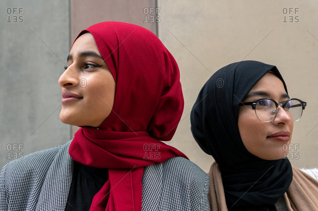 Side view of Arab female friends in traditional hijab standing on the street and looking away