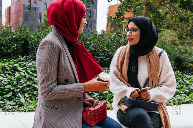 Friendly Arab female friends sitting on street and talking to each other while enjoying weekend together