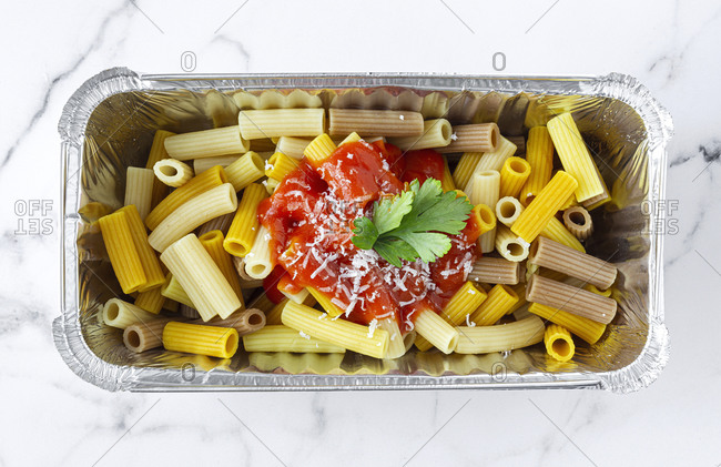 From above of delicious macaroni with ketchup and cheese placed in container for takeaway food on table