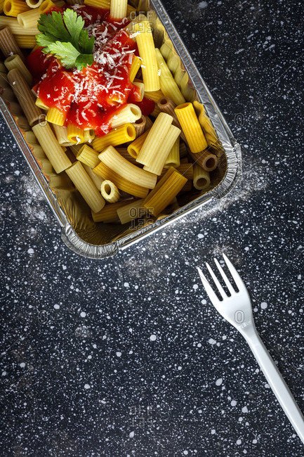 From above of delicious macaroni with ketchup and cheese placed in container for takeaway food on table with plastic fork