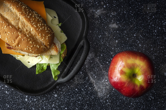 From above of delicious sandwich with cheese and lettuce placed on table with ripe apple