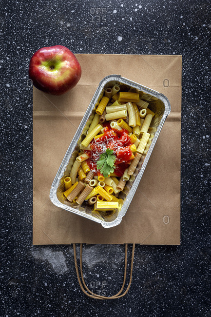 From above of delicious macaroni with ketchup and cheese placed in container for takeaway food on table with apple