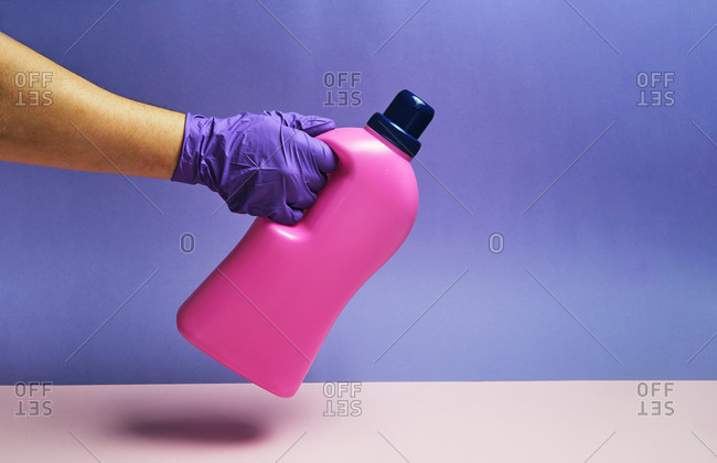 Crop anonymous person holding plastic bottle detergent on table in studio