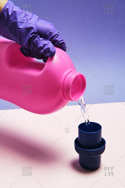 Crop anonymous person with plastic bottle pouring liquid detergent in cap placed on table in studio