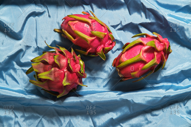 From above of whole fresh pitaya fruits arranged on blue wrinkled cloth in studio
