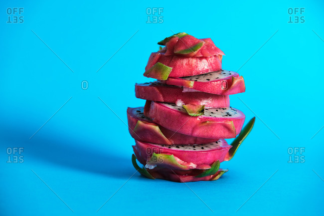 Slices of fresh delicious Dragon fruit stacked on bright blue background in studio