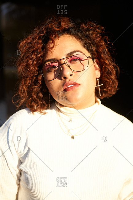 Plump female wearing trendy clothes and glasses standing in city on sunny day and confidently looking at camera