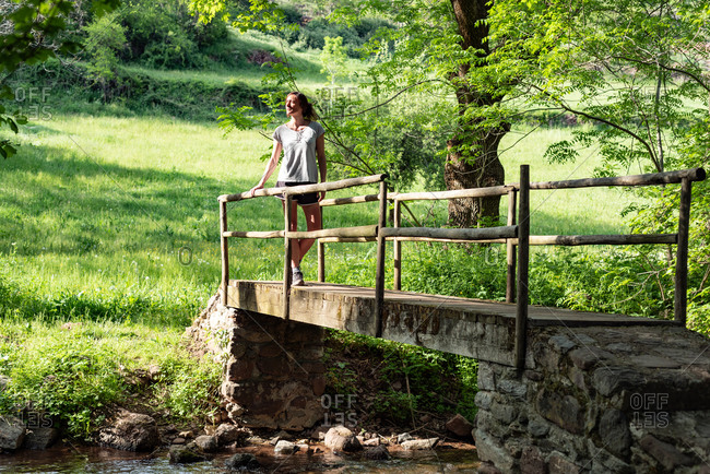 Calm female standing on old bridge over river in woods and enjoying nature in summer