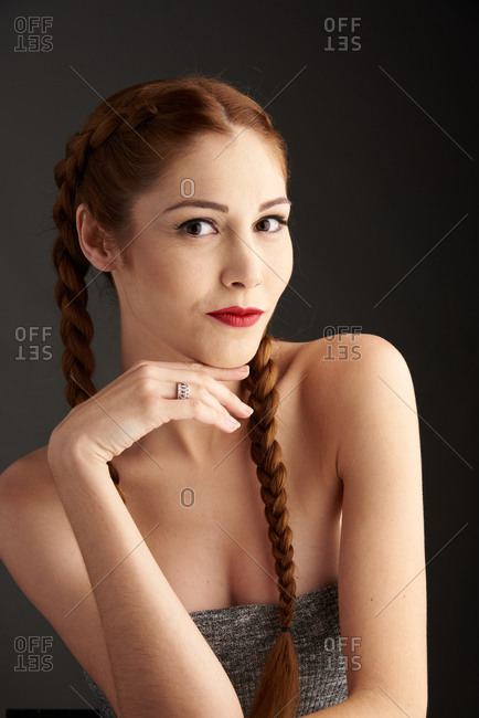 Stylish female model with red hair and braids sitting in studio on dark background and looking at camera