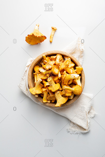Overhead view of wild mushrooms in wooden bowl on white table