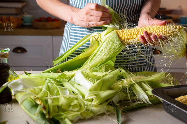 Woman shucking corn husks at domestic kitchen