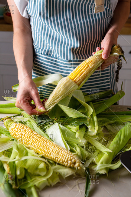 Woman shucking corn husks while cooking at home
