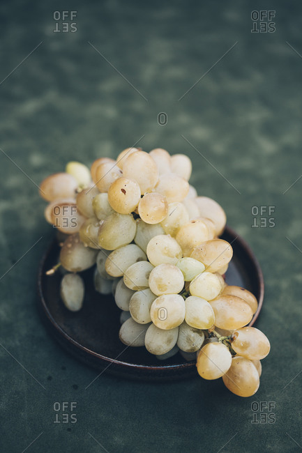Bunch of white grapes on the black plate against green background