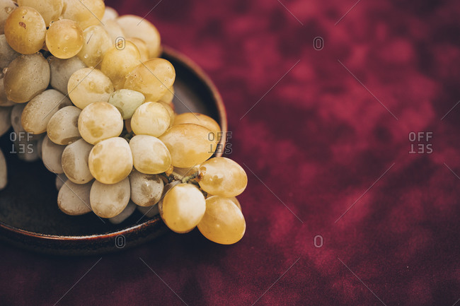 A plate filled with a bunch of white grapes on burgundy background