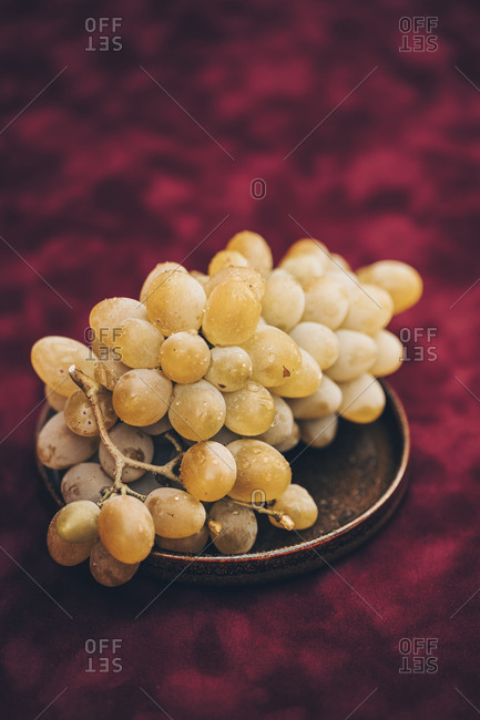 A plate filled with white grapes on burgundy background